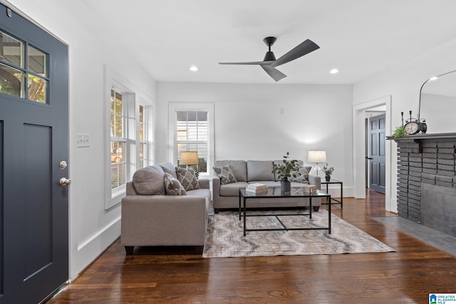 living room featuring ceiling fan, dark wood-type flooring, and a brick fireplace