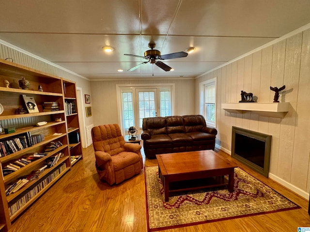 living room with ceiling fan, crown molding, a tiled fireplace, hardwood / wood-style floors, and wood walls