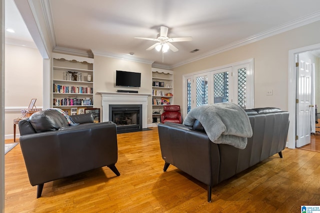 living room featuring crown molding, hardwood / wood-style flooring, ceiling fan, and built in shelves