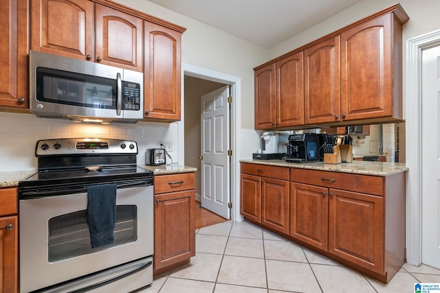 kitchen with light stone countertops, tasteful backsplash, appliances with stainless steel finishes, and light tile patterned floors