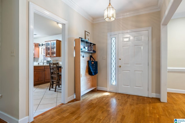 entrance foyer with crown molding, a chandelier, sink, and light wood-type flooring