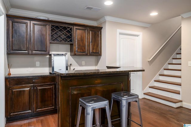 bar featuring ornamental molding, dark stone countertops, dark brown cabinets, and dark hardwood / wood-style floors