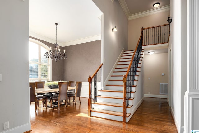 stairs with an inviting chandelier, wood-type flooring, and crown molding