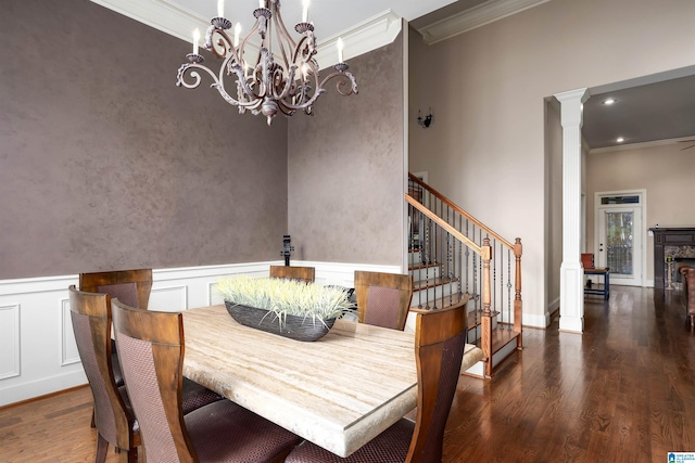 dining space featuring a fireplace, dark hardwood / wood-style flooring, ornate columns, crown molding, and a notable chandelier