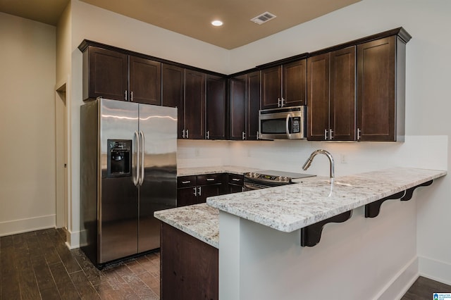 kitchen featuring light stone countertops, sink, appliances with stainless steel finishes, dark hardwood / wood-style flooring, and dark brown cabinetry