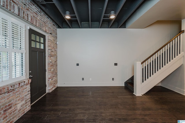 foyer entrance featuring a towering ceiling, brick wall, and dark wood-type flooring