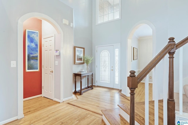 foyer entrance with arched walkways, baseboards, wood finished floors, a high ceiling, and stairway