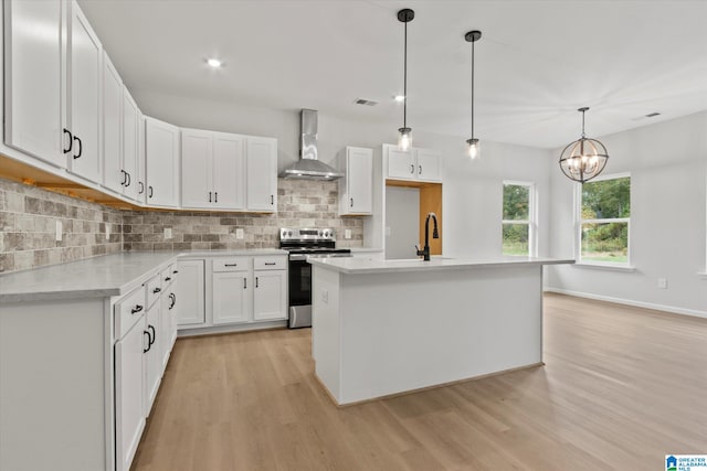 kitchen featuring white cabinetry, wall chimney exhaust hood, stainless steel electric range, pendant lighting, and a center island with sink