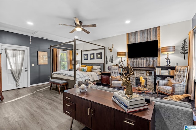 bedroom featuring light wood-type flooring, ceiling fan, and a stone fireplace