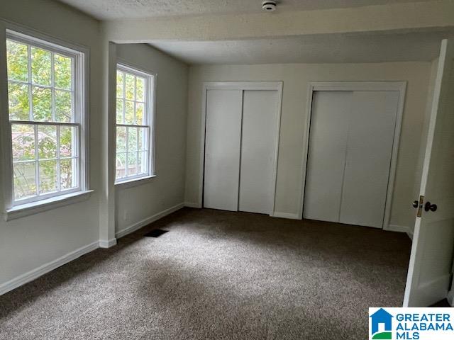 unfurnished bedroom with a textured ceiling, two closets, and carpet