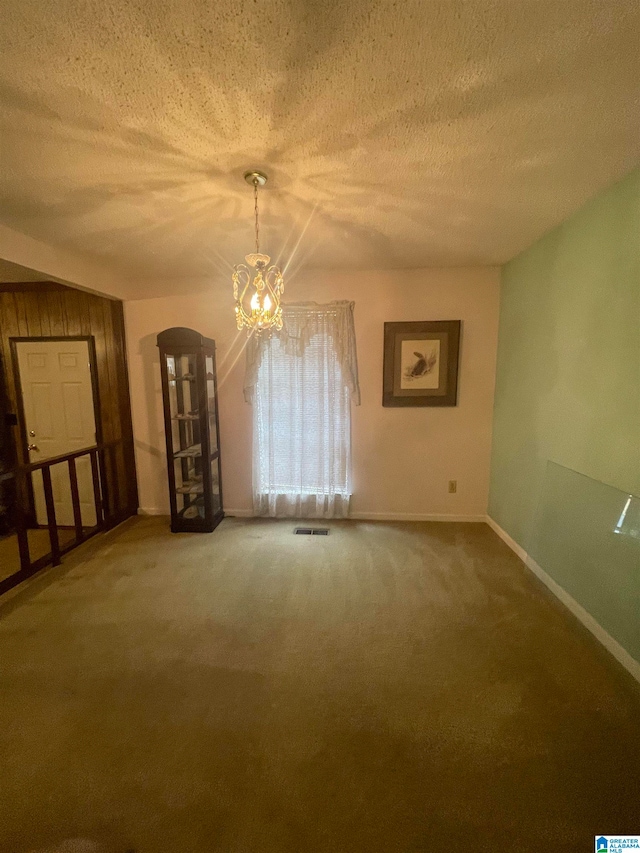 spare room featuring carpet, wood walls, a textured ceiling, and an inviting chandelier