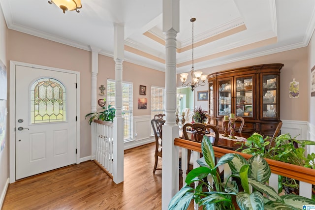 entrance foyer featuring crown molding, ornate columns, a raised ceiling, an inviting chandelier, and hardwood / wood-style floors