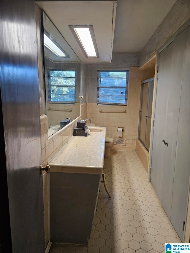 bathroom featuring toilet, tile patterned flooring, a shower with shower door, vanity, and tile walls