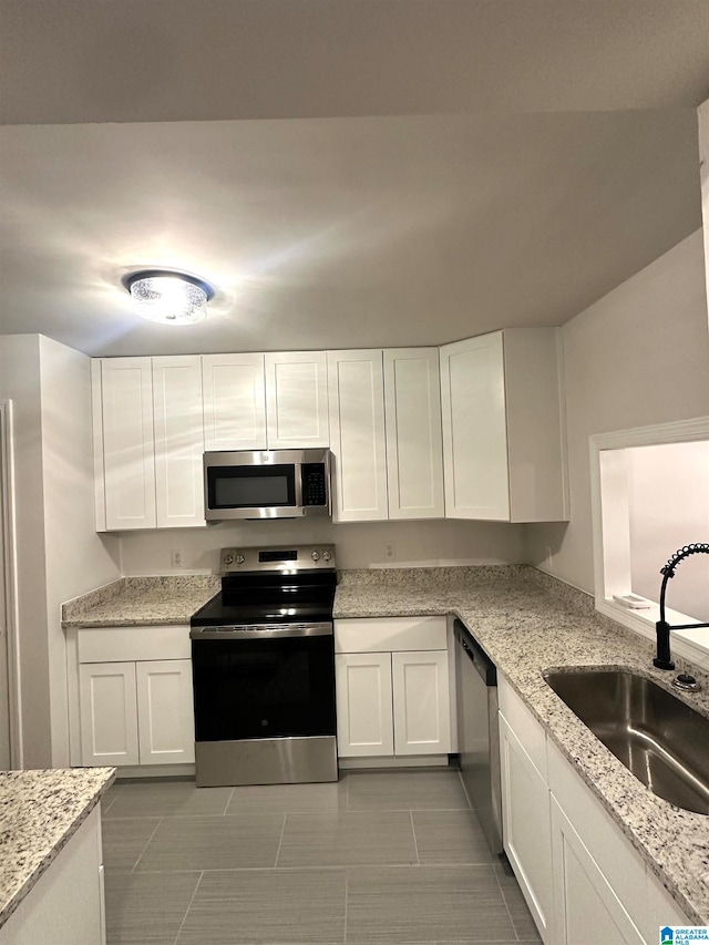 kitchen with white cabinetry, light stone counters, stainless steel appliances, and sink