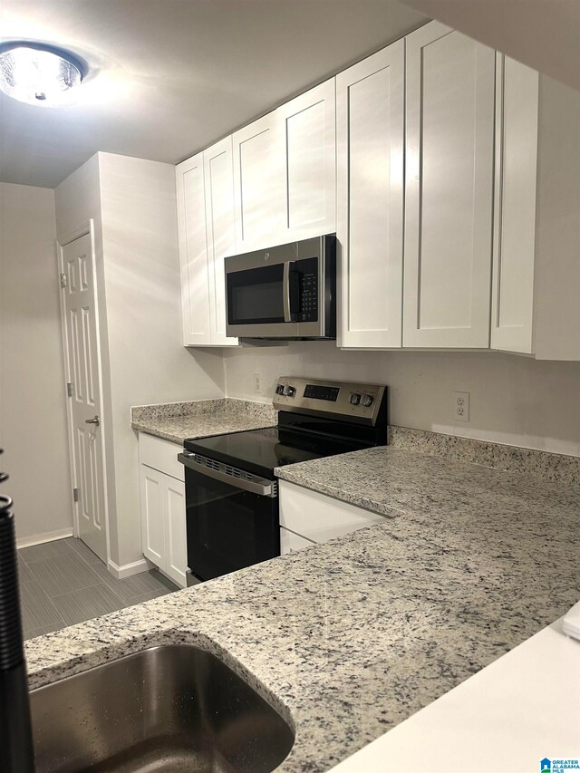 kitchen featuring light stone countertops, white cabinetry, stainless steel appliances, and light tile patterned floors