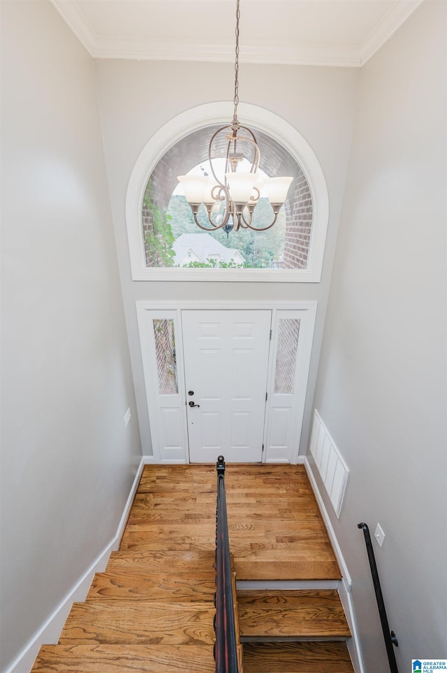 entryway with a chandelier, wood-type flooring, crown molding, and a high ceiling