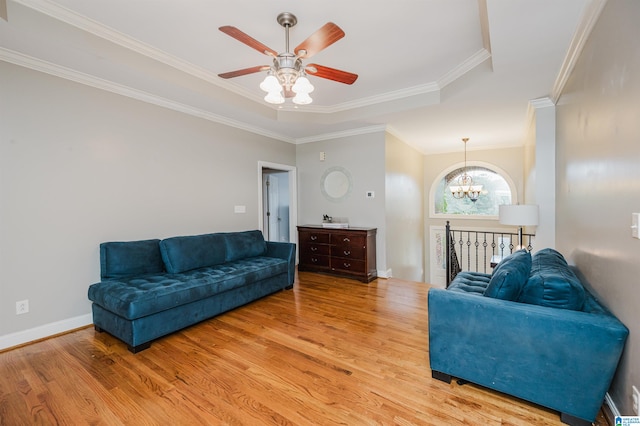 living room with a raised ceiling, crown molding, light hardwood / wood-style floors, and ceiling fan with notable chandelier