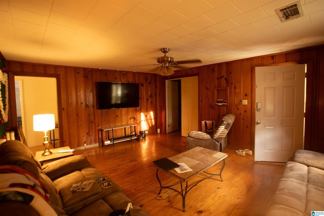 living room featuring ceiling fan, wood-type flooring, and wooden walls