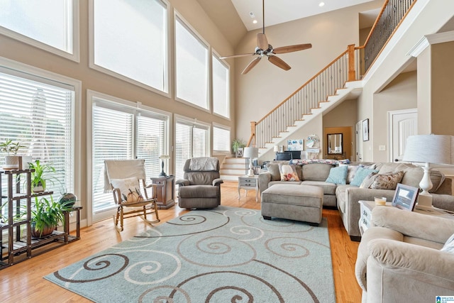 living room featuring a towering ceiling, ceiling fan, plenty of natural light, and light hardwood / wood-style floors