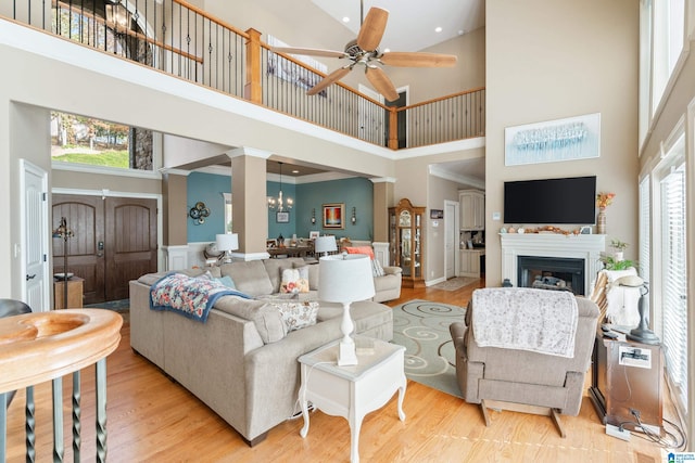 living room featuring decorative columns, ornamental molding, ceiling fan with notable chandelier, a towering ceiling, and light hardwood / wood-style floors