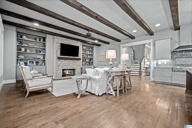 living room featuring beamed ceiling, light hardwood / wood-style floors, a stone fireplace, and built in features