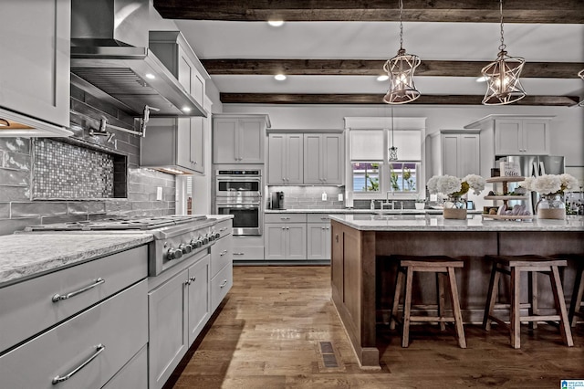 kitchen featuring wall chimney range hood, stainless steel appliances, light stone countertops, pendant lighting, and dark hardwood / wood-style flooring