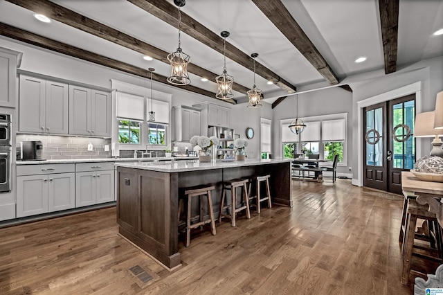 kitchen featuring dark hardwood / wood-style flooring, beam ceiling, decorative light fixtures, and an island with sink