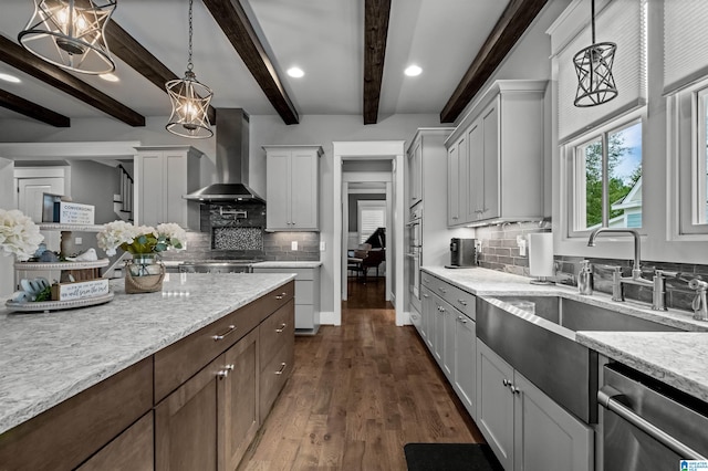 kitchen with light stone countertops, stainless steel appliances, wall chimney exhaust hood, beamed ceiling, and pendant lighting