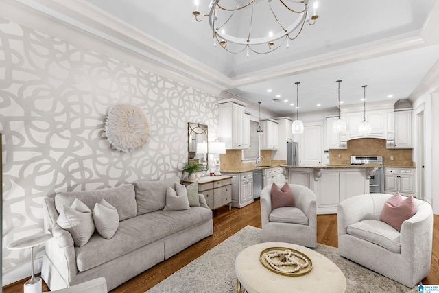 living room with a notable chandelier, hardwood / wood-style flooring, sink, and crown molding