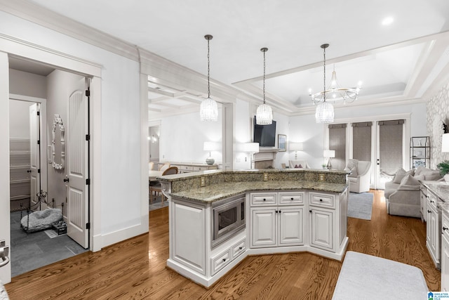 kitchen with stainless steel microwave, white cabinets, hardwood / wood-style flooring, and hanging light fixtures