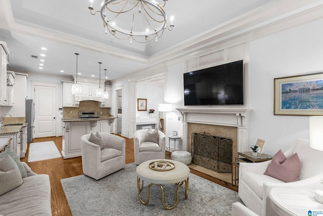 living room with a high end fireplace, a notable chandelier, light hardwood / wood-style floors, and a raised ceiling