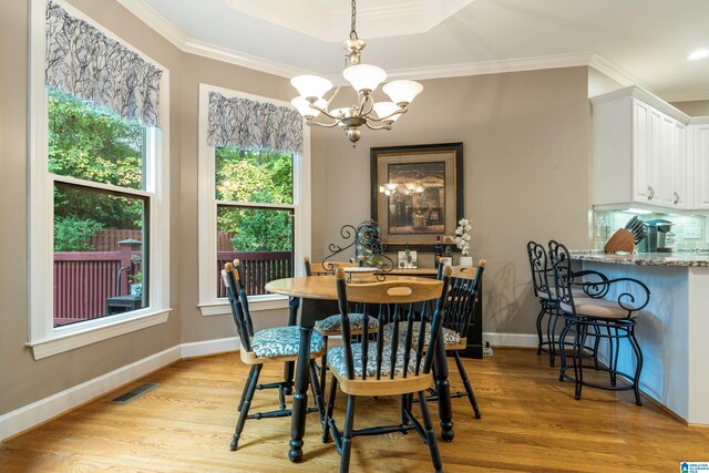 dining space featuring ornamental molding, a notable chandelier, light hardwood / wood-style floors, and a raised ceiling