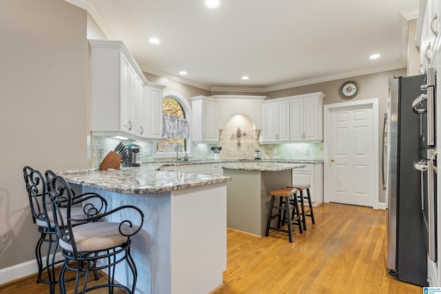 kitchen with light hardwood / wood-style flooring, stainless steel refrigerator, white cabinets, and a breakfast bar area