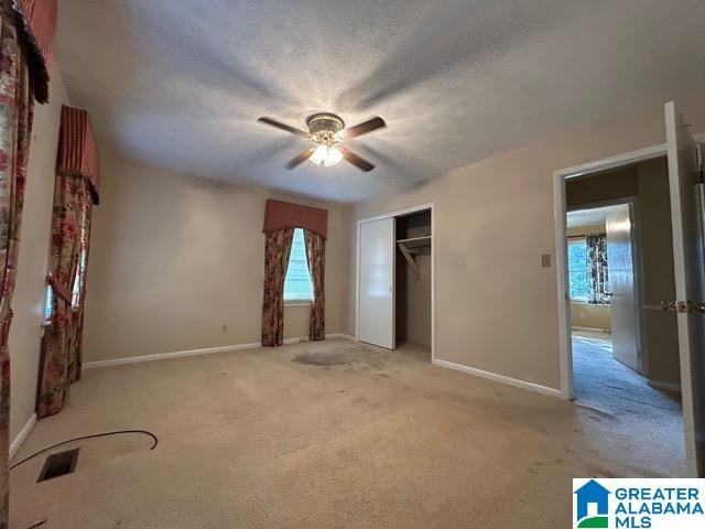 unfurnished bedroom featuring light colored carpet, multiple windows, a closet, and ceiling fan