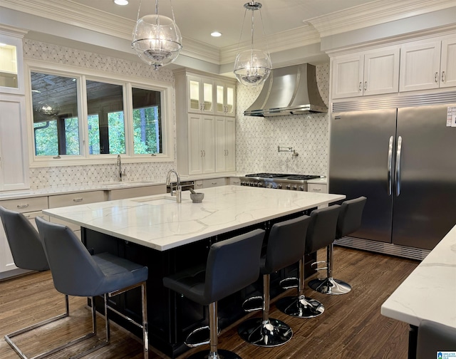 kitchen with a healthy amount of sunlight, an island with sink, stainless steel appliances, and wall chimney range hood