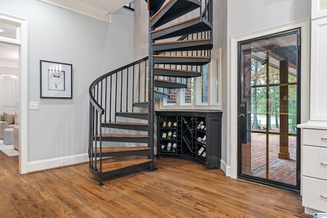 staircase with ornamental molding, wood finished floors, and baseboards