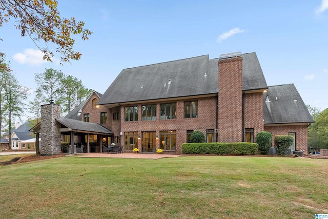 rear view of property with a patio area, a chimney, a lawn, and brick siding