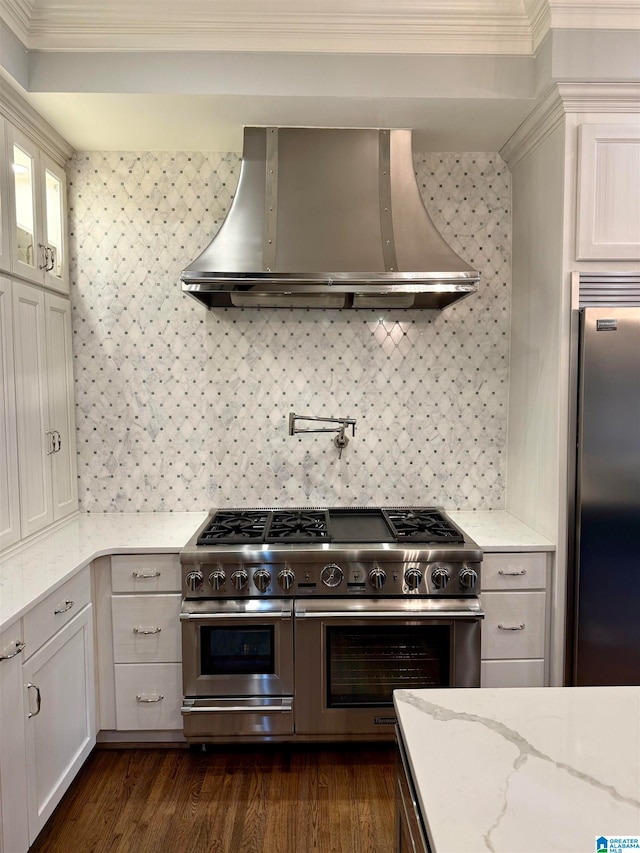 kitchen with premium appliances, light stone counters, wall chimney range hood, dark wood finished floors, and crown molding