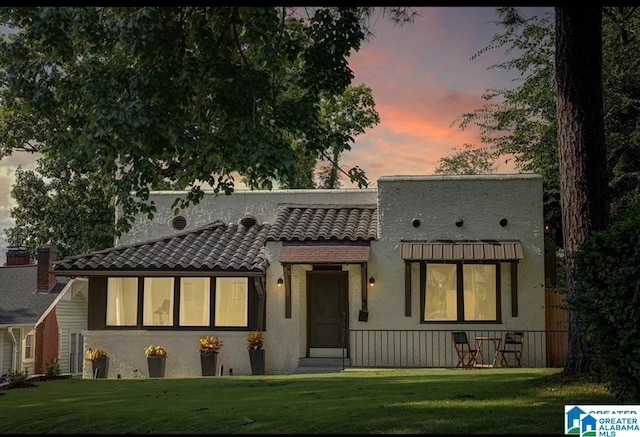 back house at dusk featuring a lawn