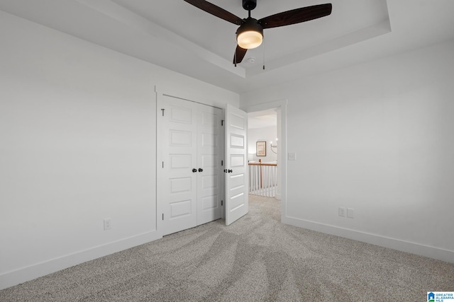 unfurnished bedroom with a closet, ceiling fan, a raised ceiling, and carpet floors