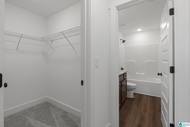 interior space with vanity, toilet, hardwood / wood-style flooring, and shower / tub combination