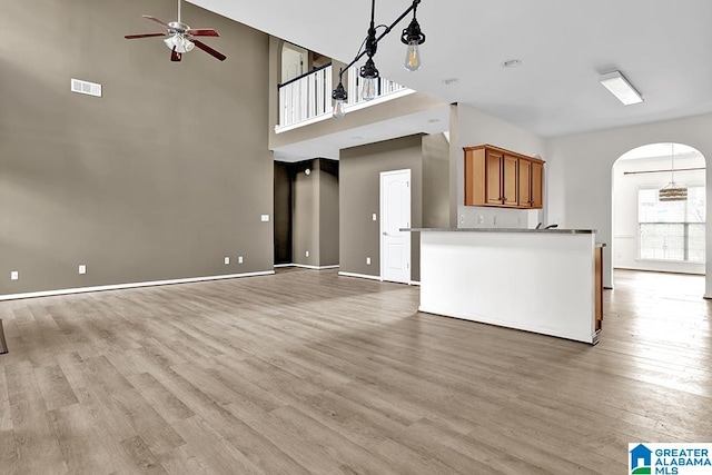 unfurnished living room with light hardwood / wood-style flooring, a towering ceiling, and ceiling fan