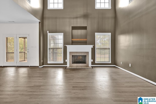 unfurnished living room with a towering ceiling, hardwood / wood-style floors, and a tiled fireplace