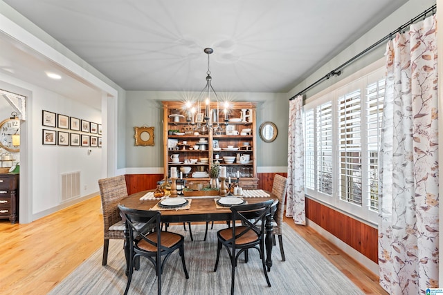 dining area featuring light hardwood / wood-style flooring, wooden walls, and an inviting chandelier