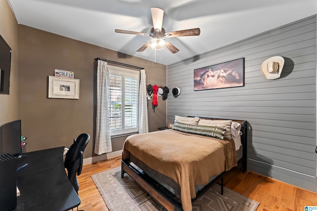 bedroom featuring light hardwood / wood-style floors, wooden walls, and ceiling fan