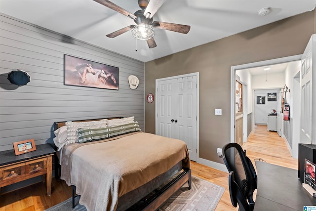 bedroom featuring wood walls, a closet, light wood-type flooring, and ceiling fan