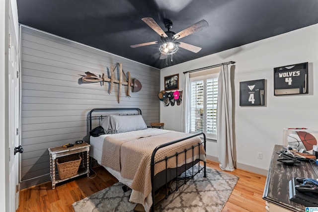 bedroom featuring wooden walls, light hardwood / wood-style floors, and ceiling fan