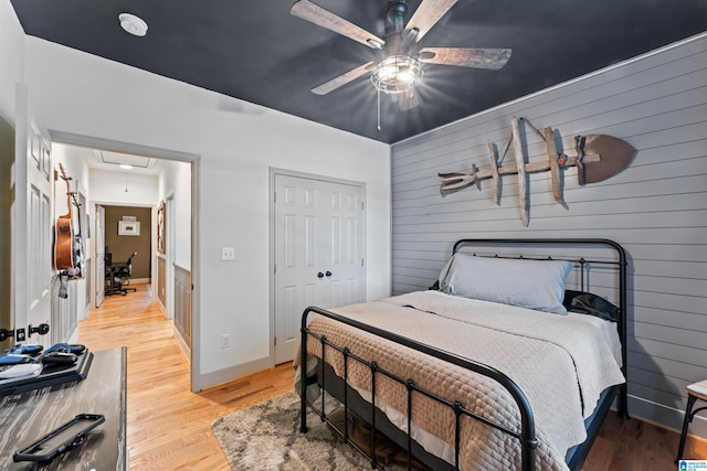 bedroom featuring light hardwood / wood-style floors, a closet, wood walls, and ceiling fan