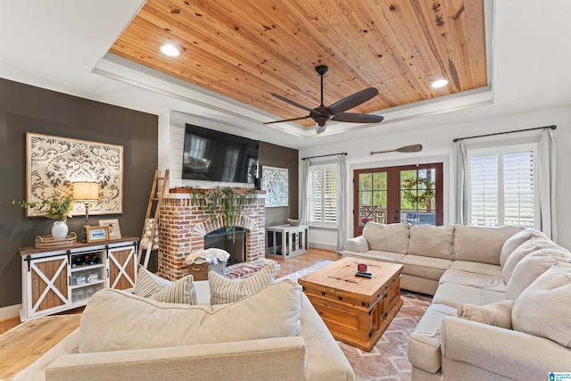 living room with light wood-type flooring, wood ceiling, a tray ceiling, a brick fireplace, and ceiling fan