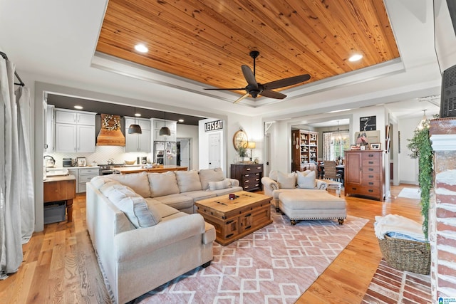 living room featuring light hardwood / wood-style flooring, sink, a tray ceiling, and ceiling fan with notable chandelier